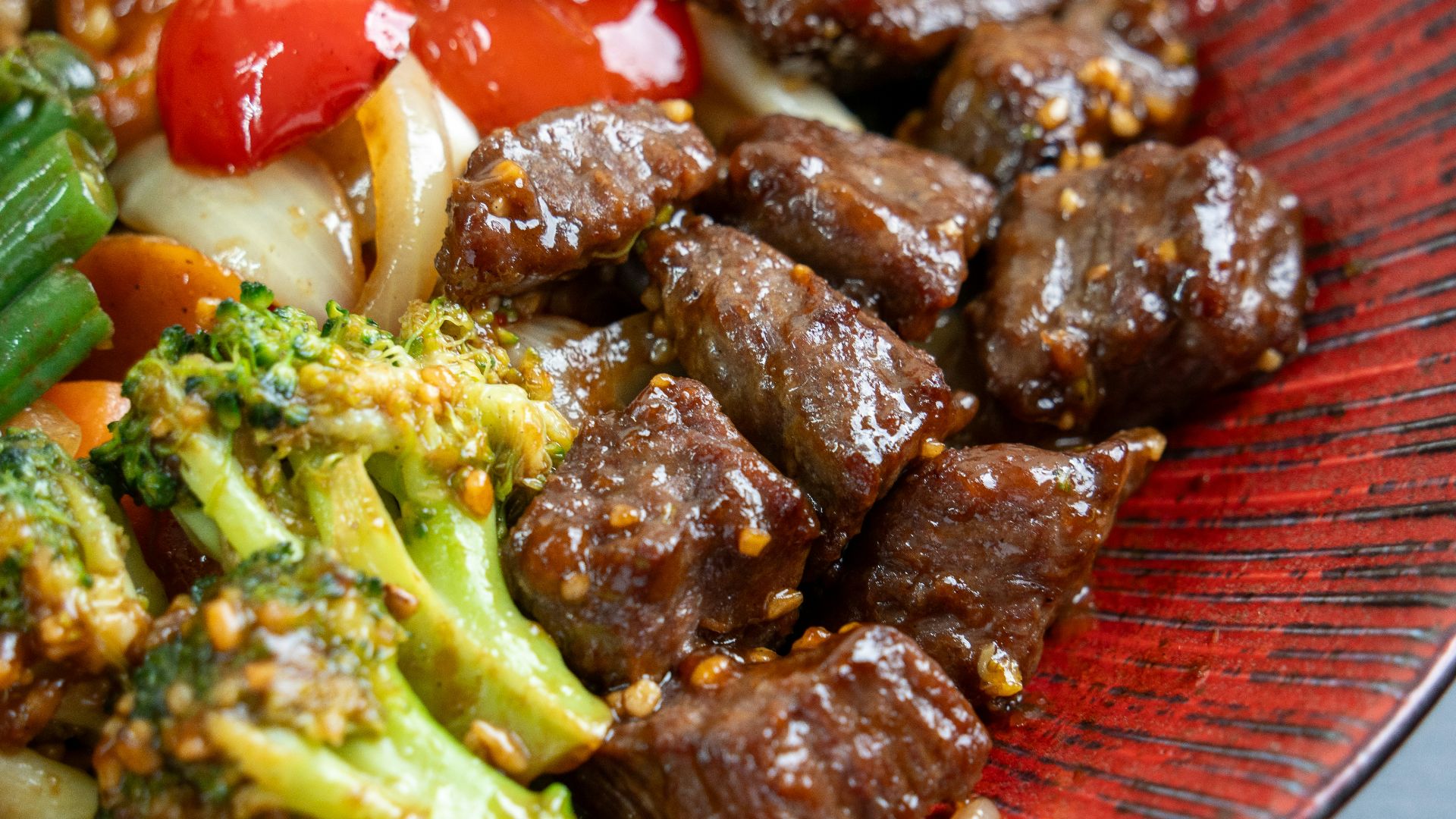 Beef and broccoli stir-fry with vegetables on a red plate