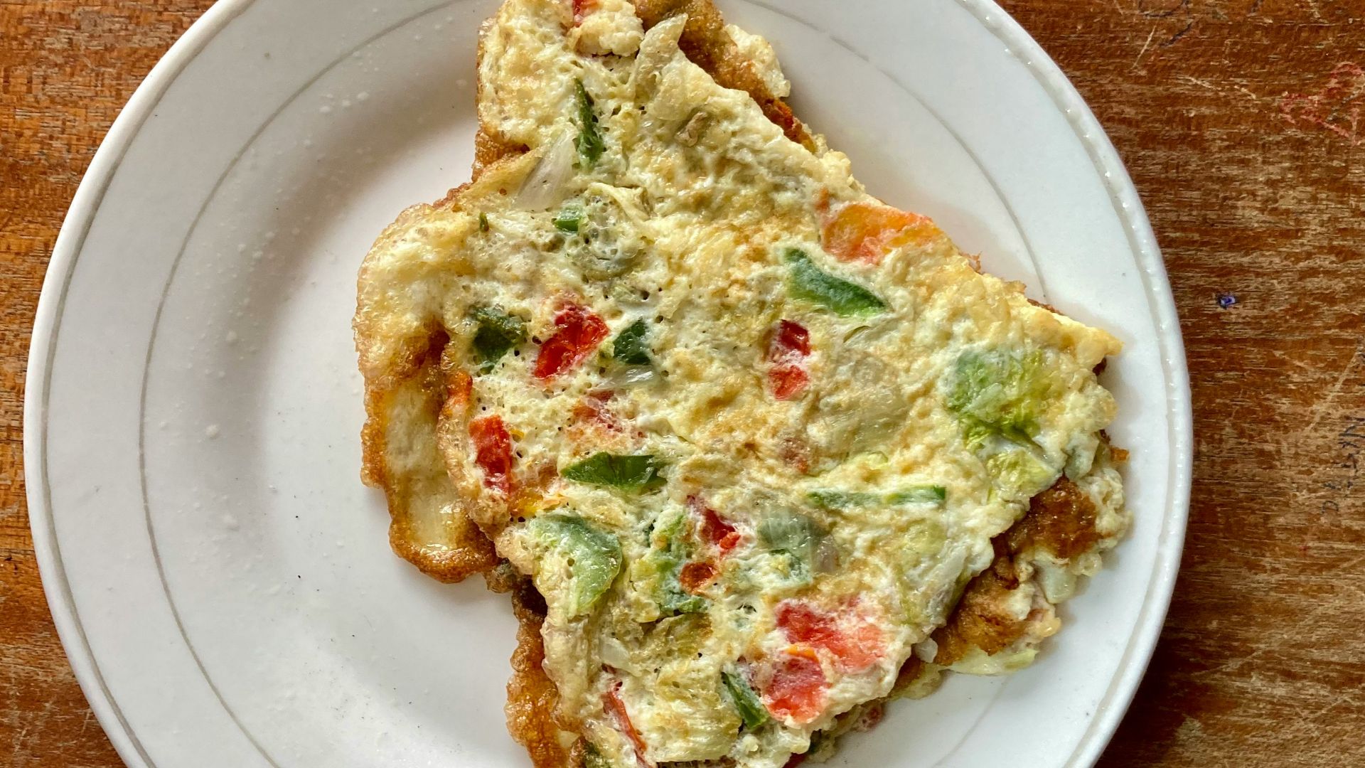 a slice of quiche on a white plate on a wooden table