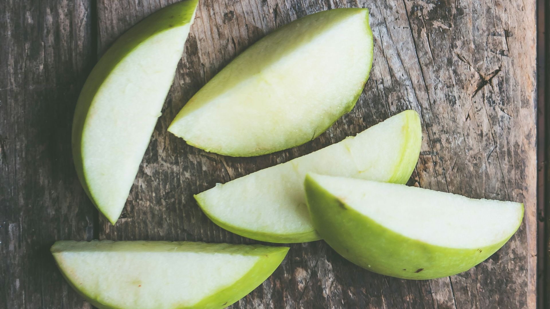 five green apple slices on brown wooden panel