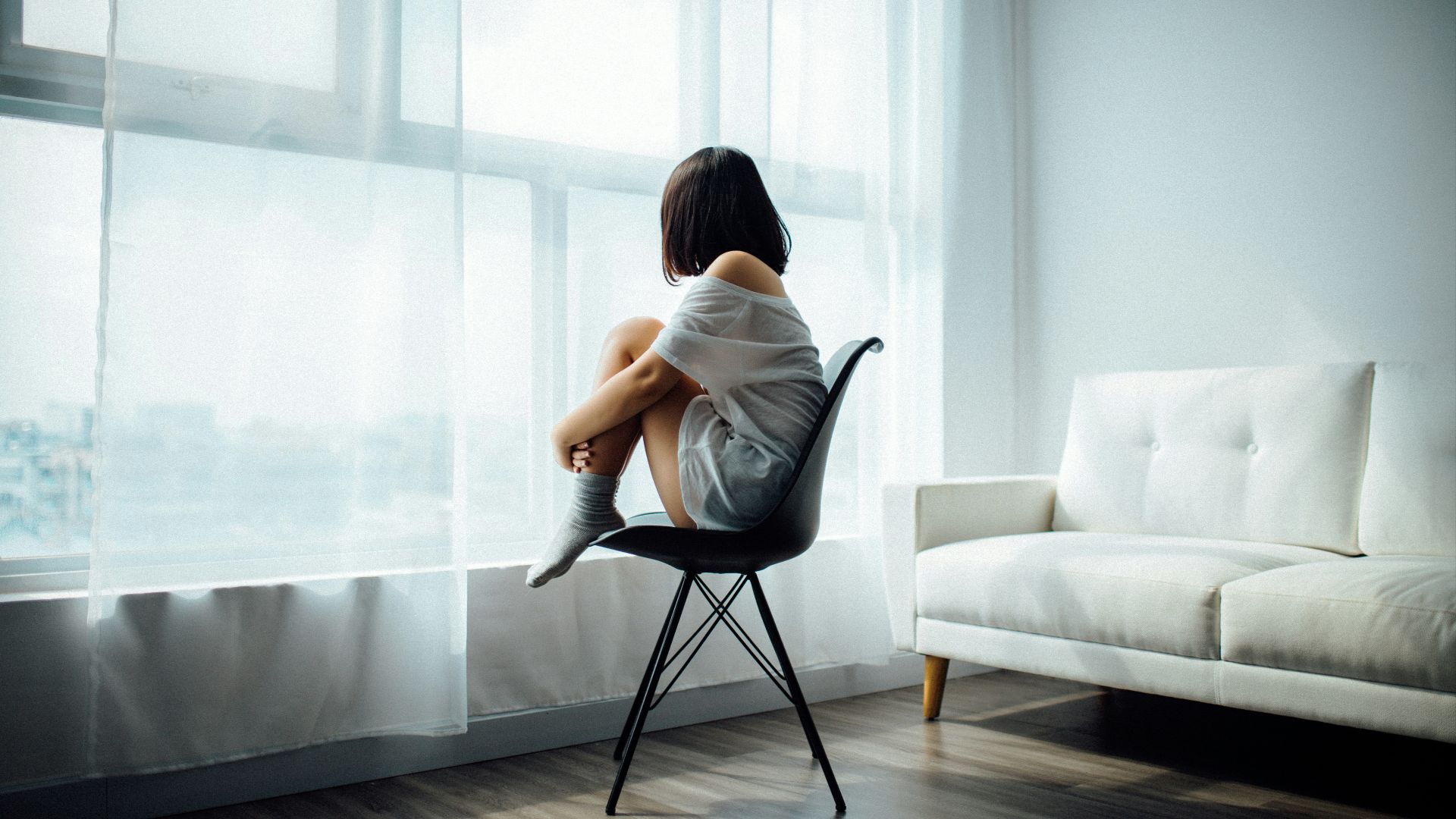 woman sitting on black chair in front of glass-panel window with white curtains