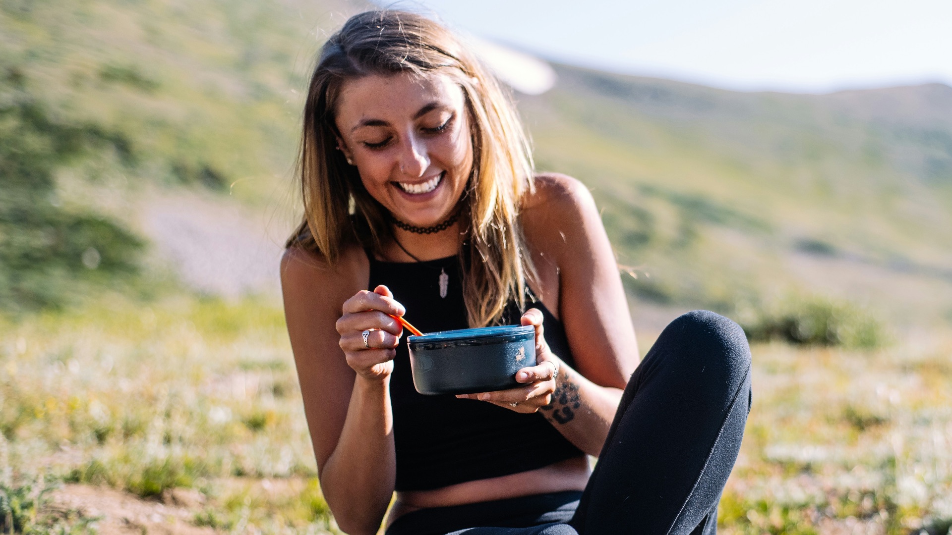 woman in black tank top and black pants sitting on ground holding blue ceramic mug during