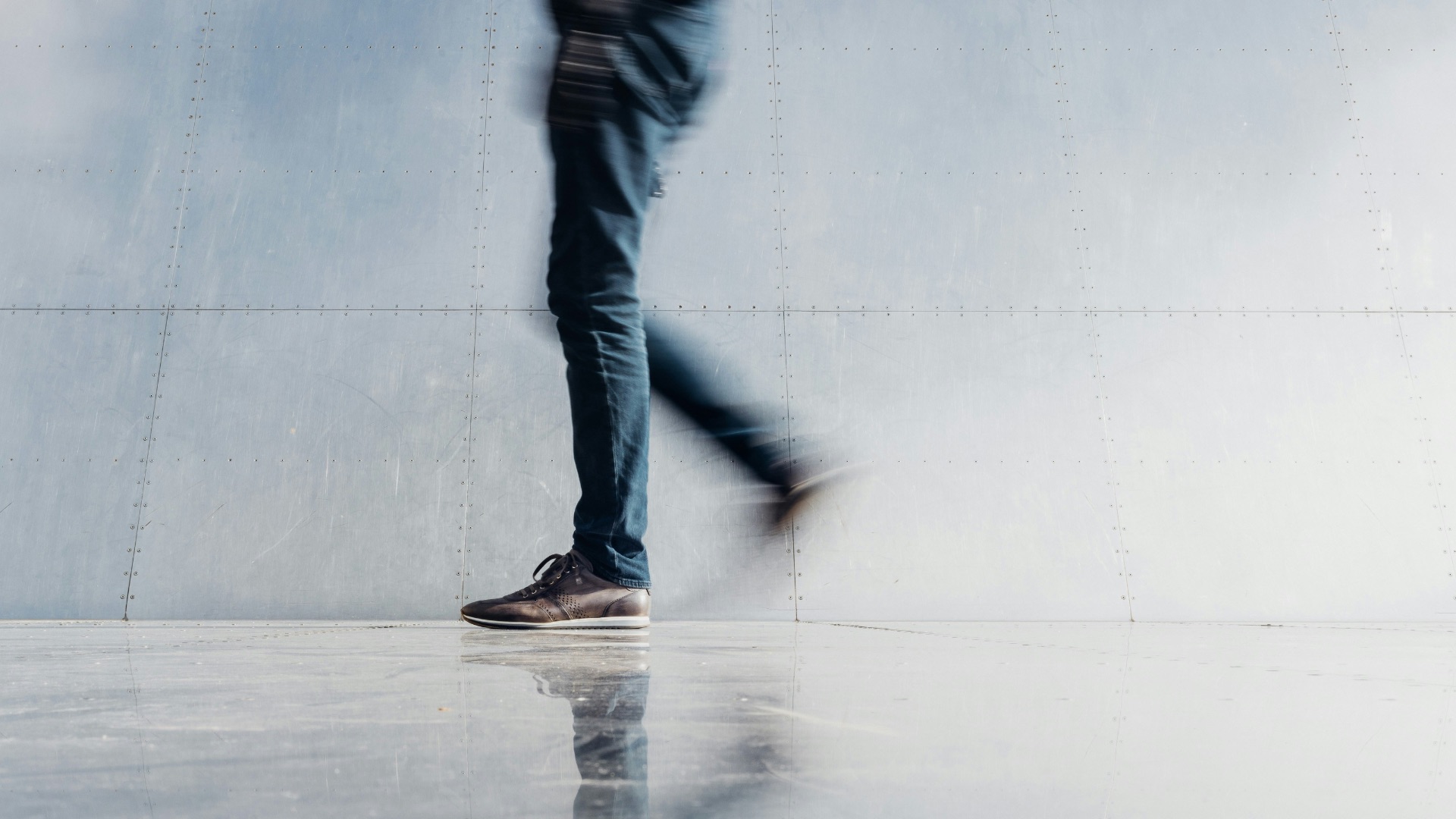 person wearing blue denim jeans beside gray wall