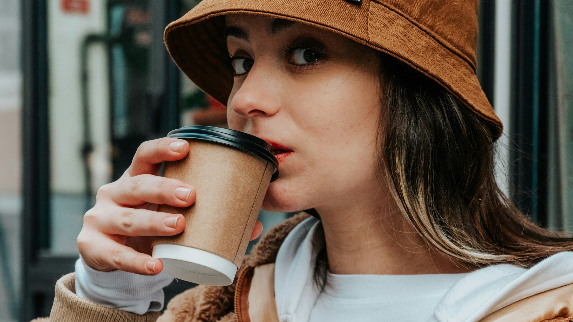 woman in brown coat holding white ceramic mug