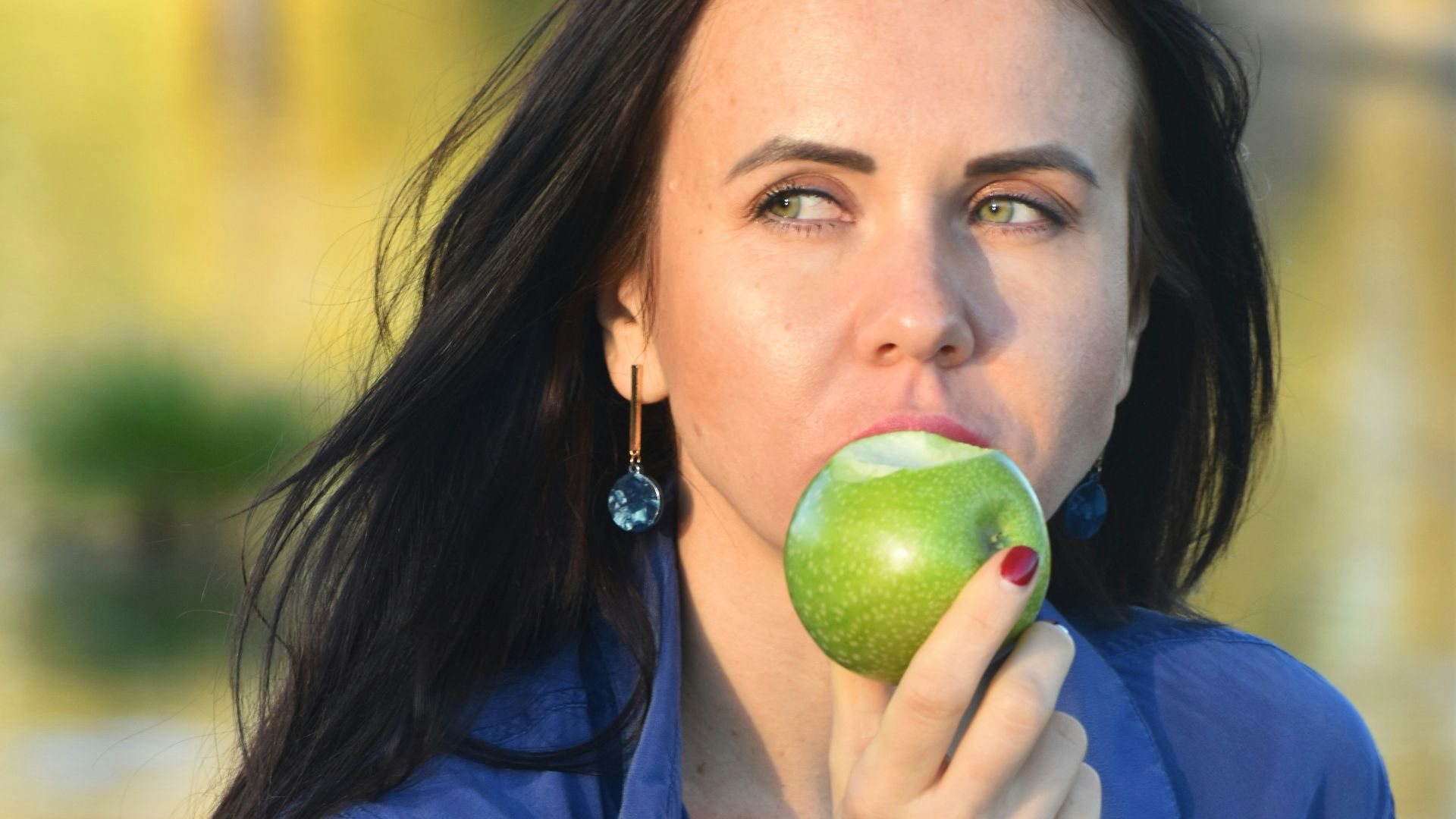 a woman in a blue shirt eating an apple