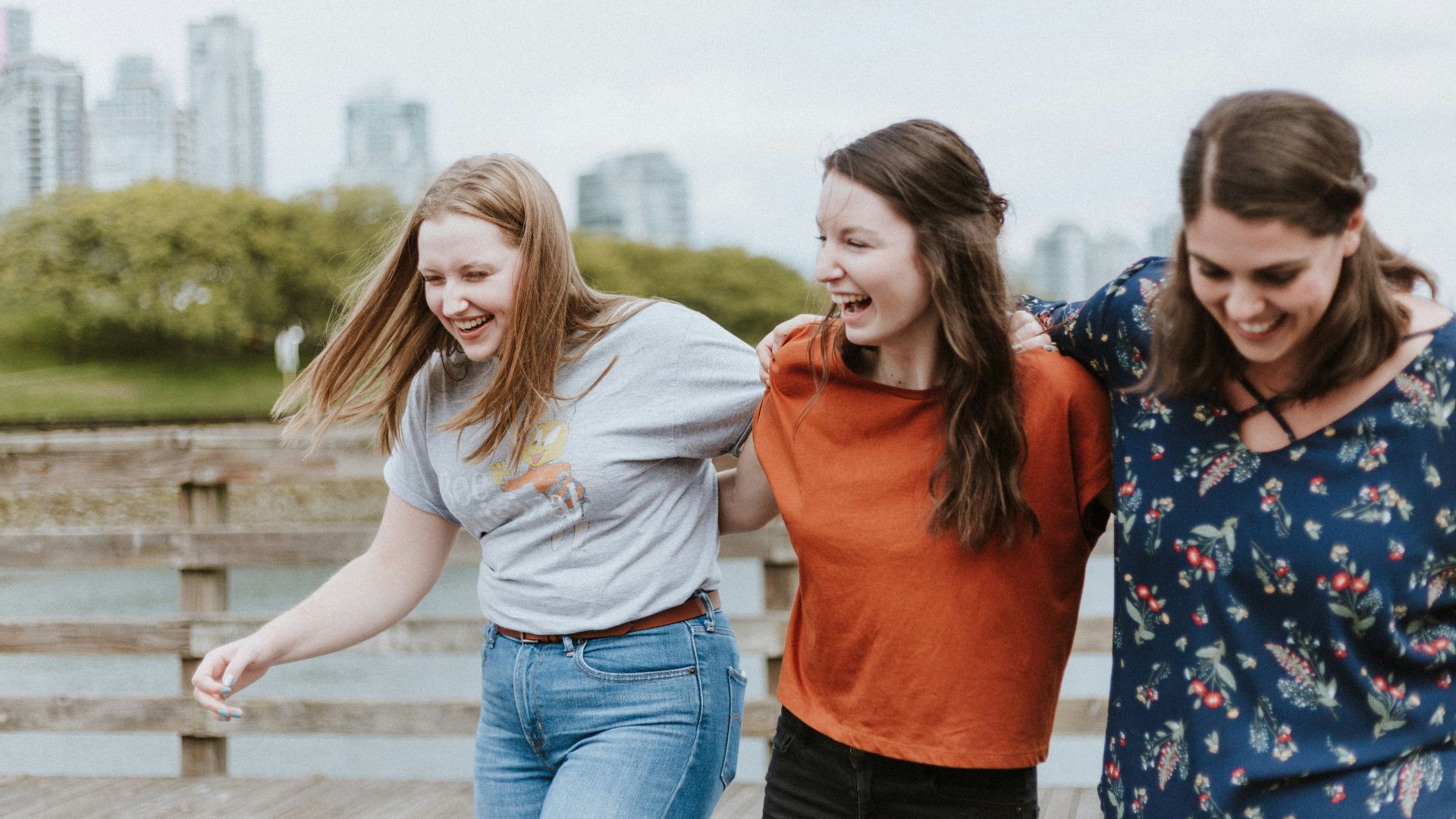three women walking on brown wooden dock near high rise building during daytime