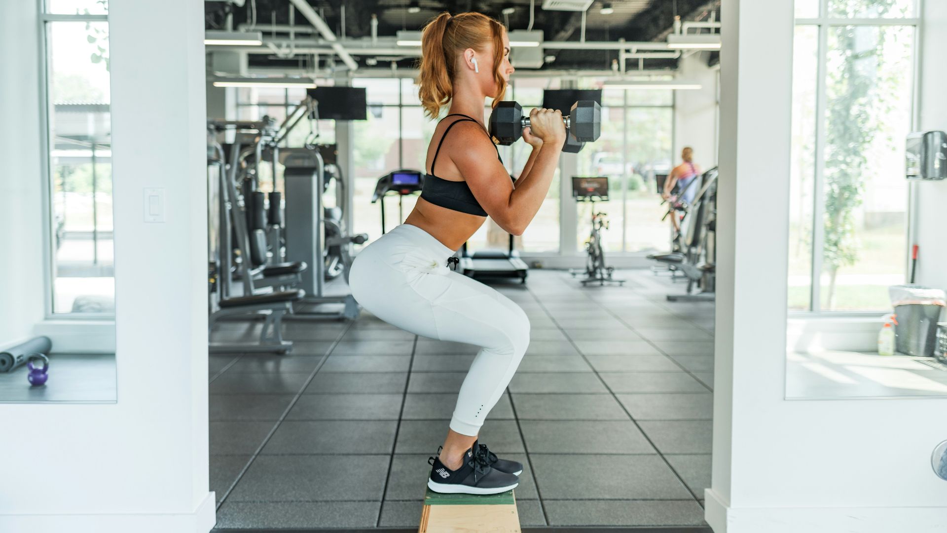 woman wearing black sports bra and white legging lifting dummbells
