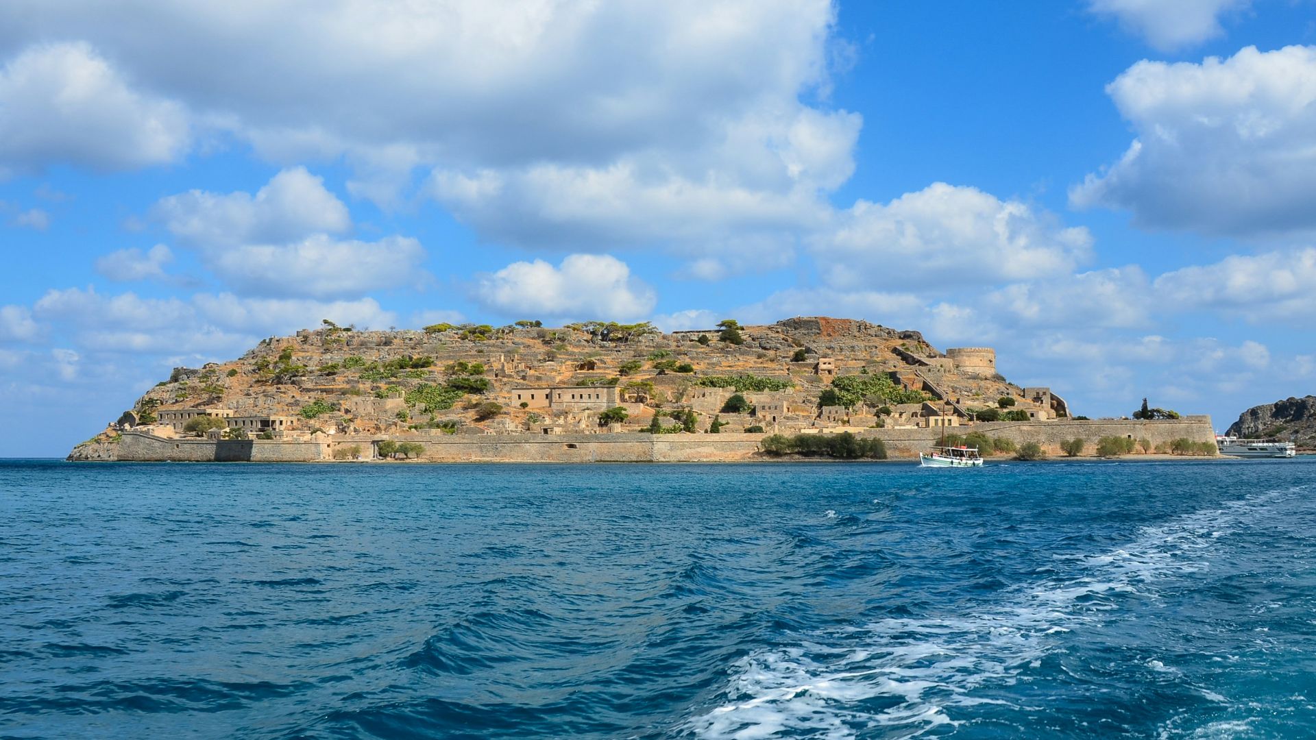 body of water near brown and green mountain under blue and white sunny cloudy sky during