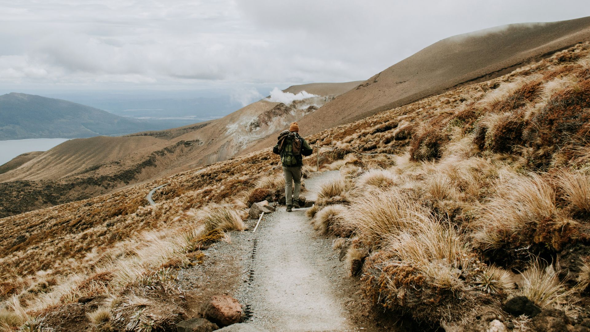 people walking on pathway near brown mountain under white clouds during daytime