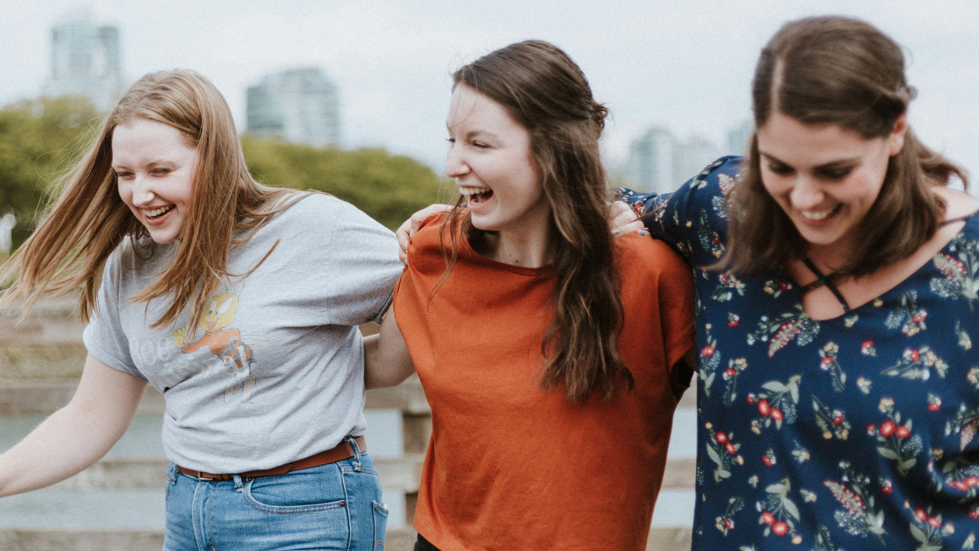 three women walking on brown wooden dock near high rise building during daytime