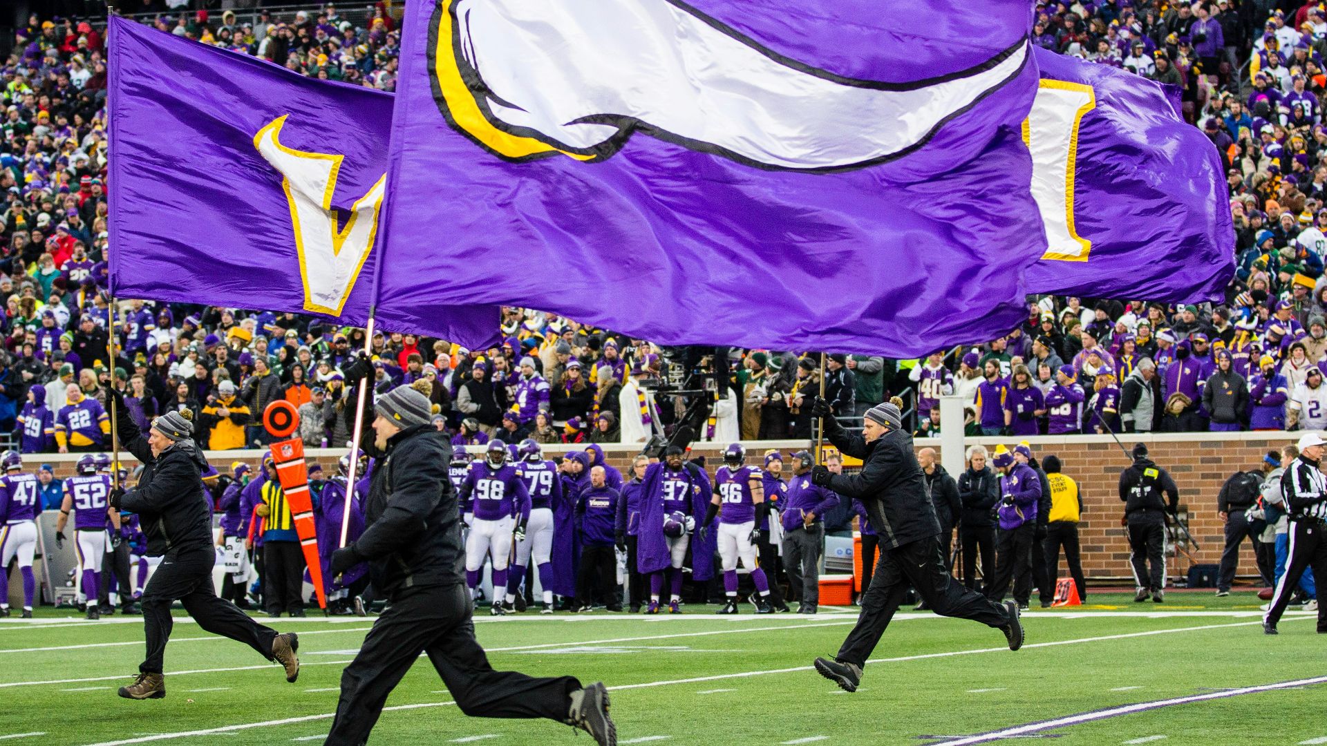 people running and holding Minnesota Vikings flags in green field