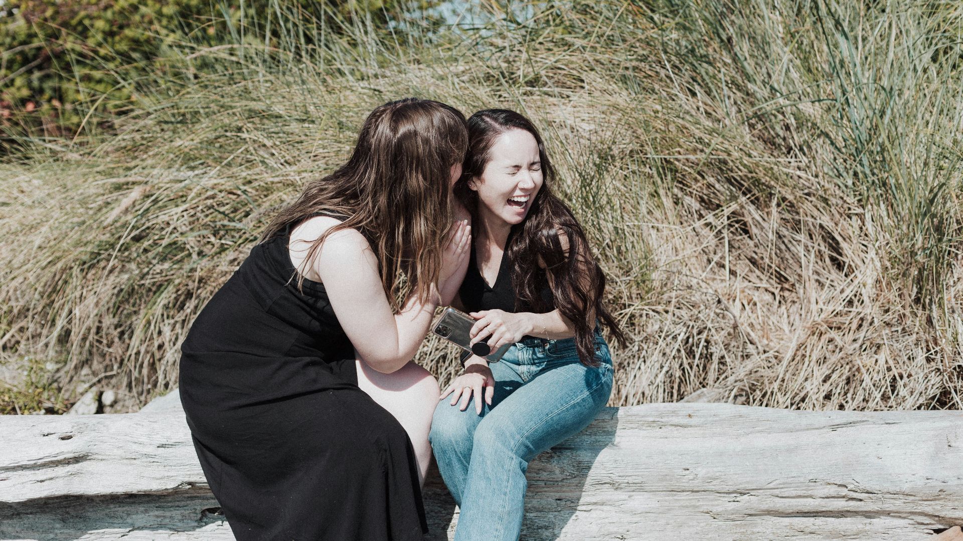 two women sitting on a log talking to each other
