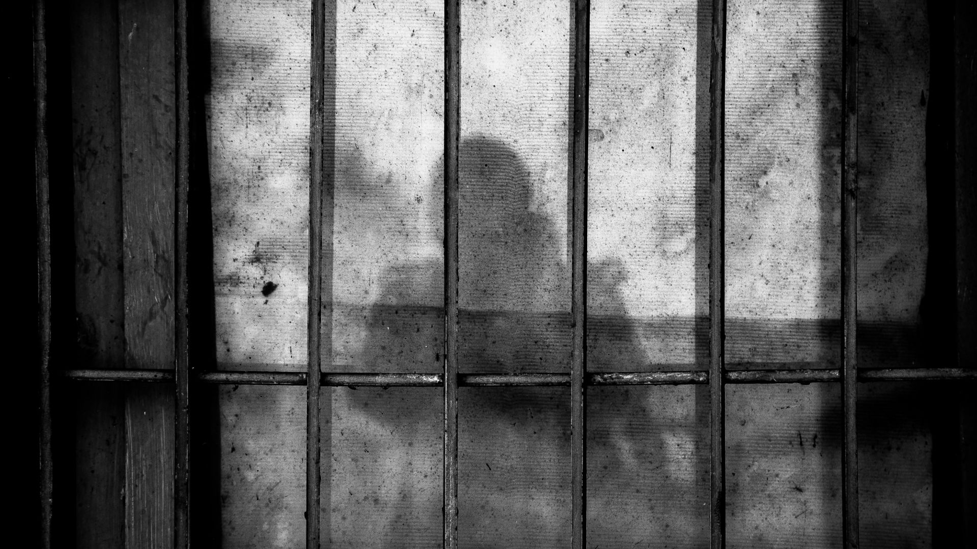a shadow of a person behind bars in a jail cell