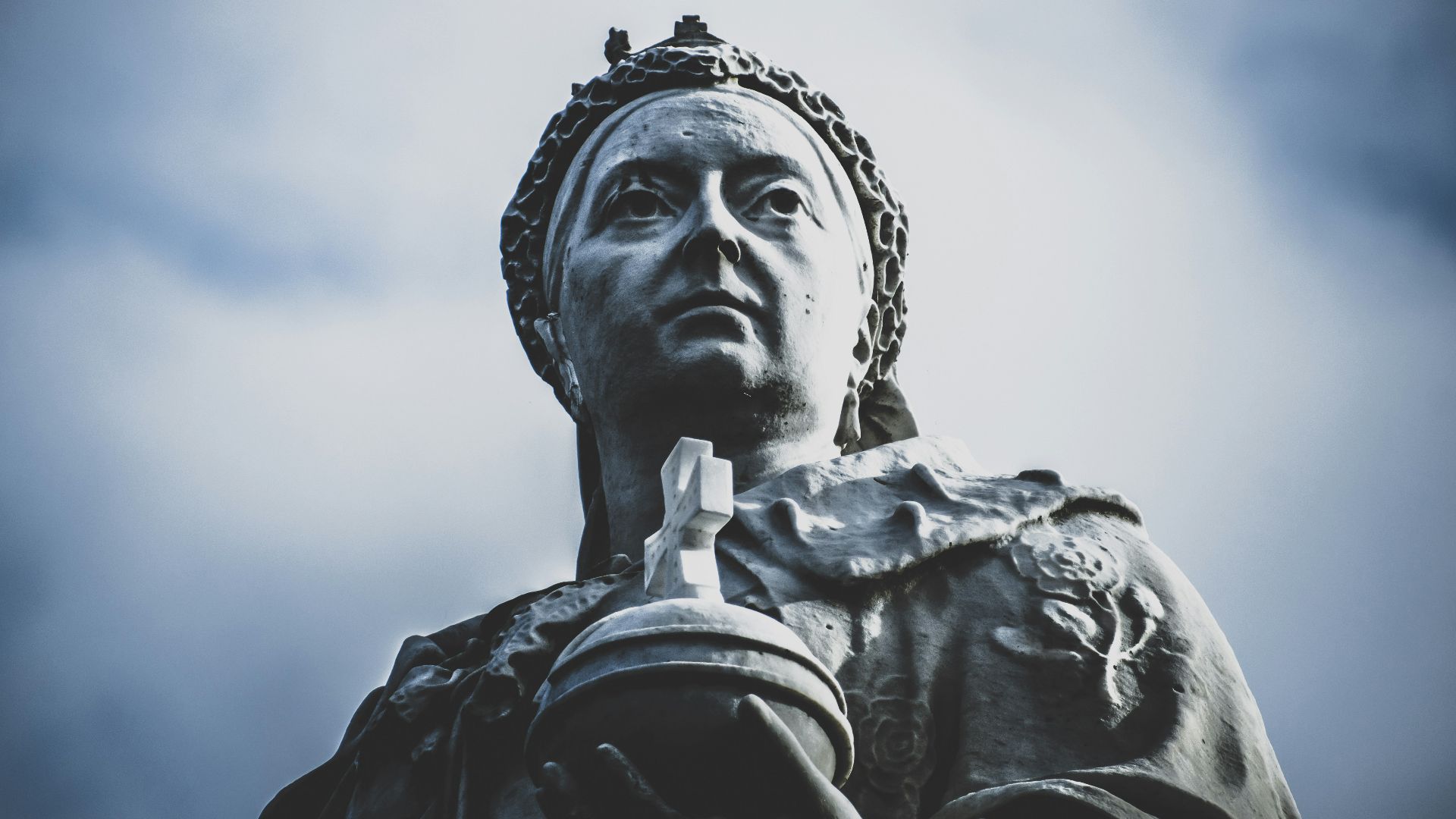 low-angle photography of woman holding cross statue under white and blue sky during daytime