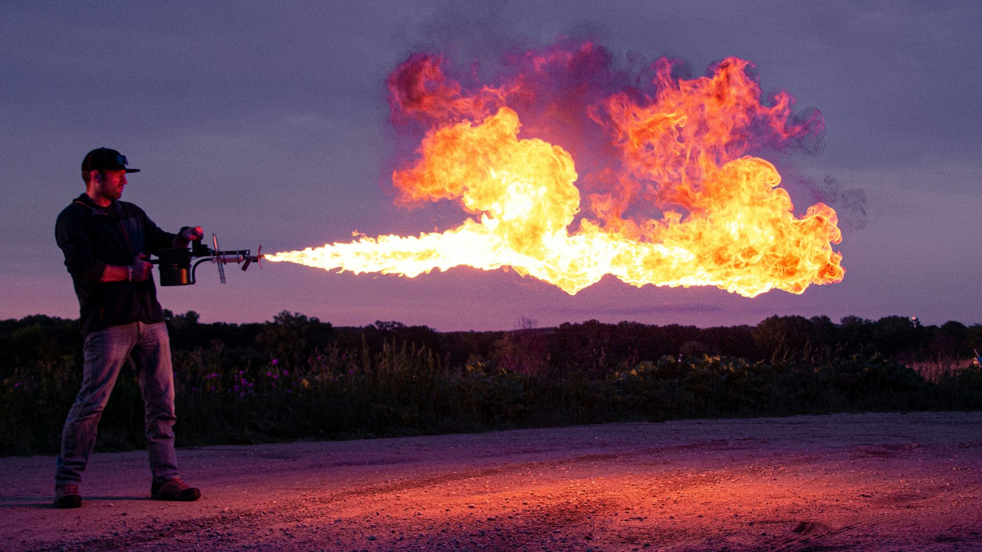 a man holding a gun and standing in front of a fire