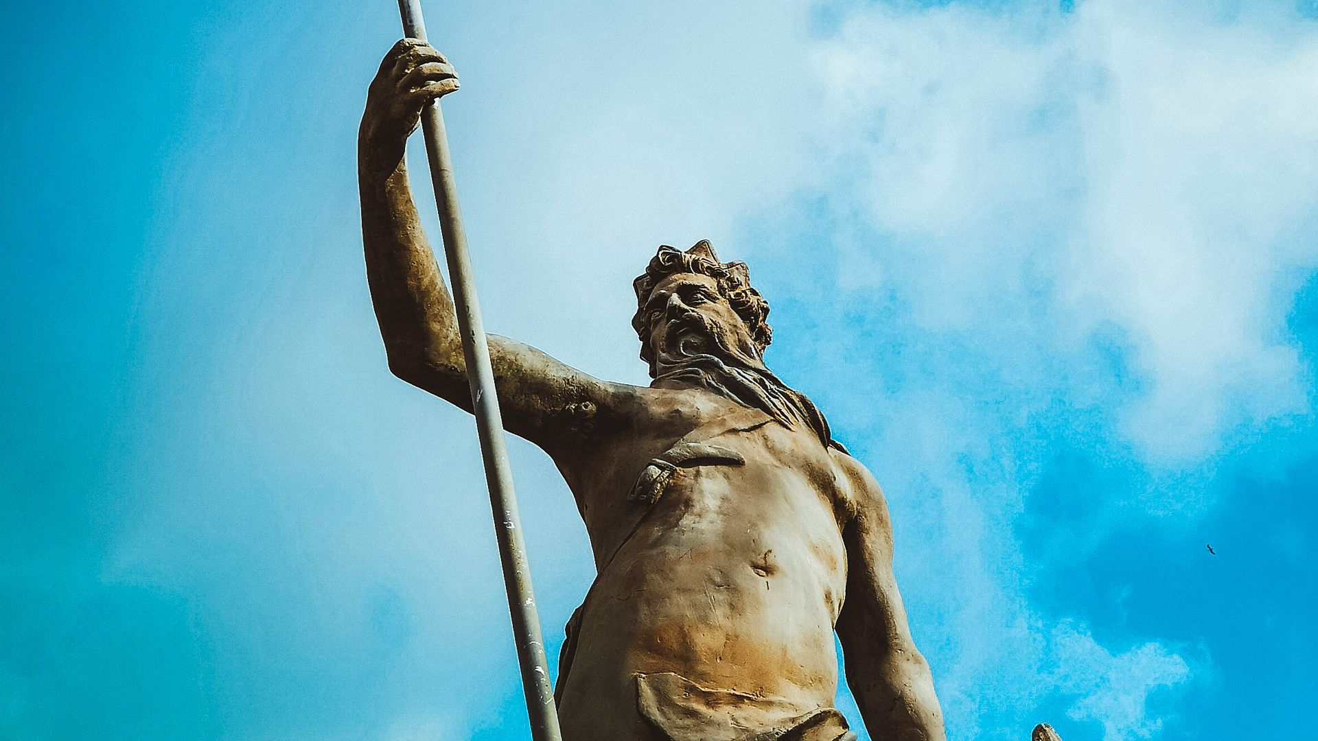man holding trident statue under white clouds at daytime