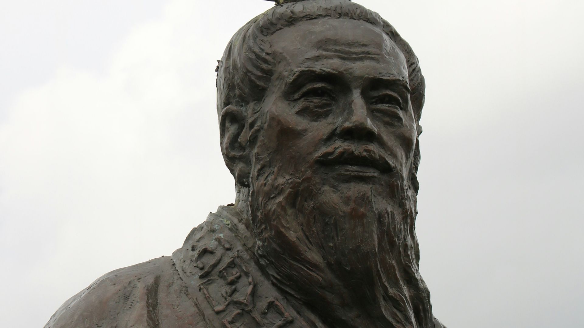 man in hat statue under white clouds during daytime