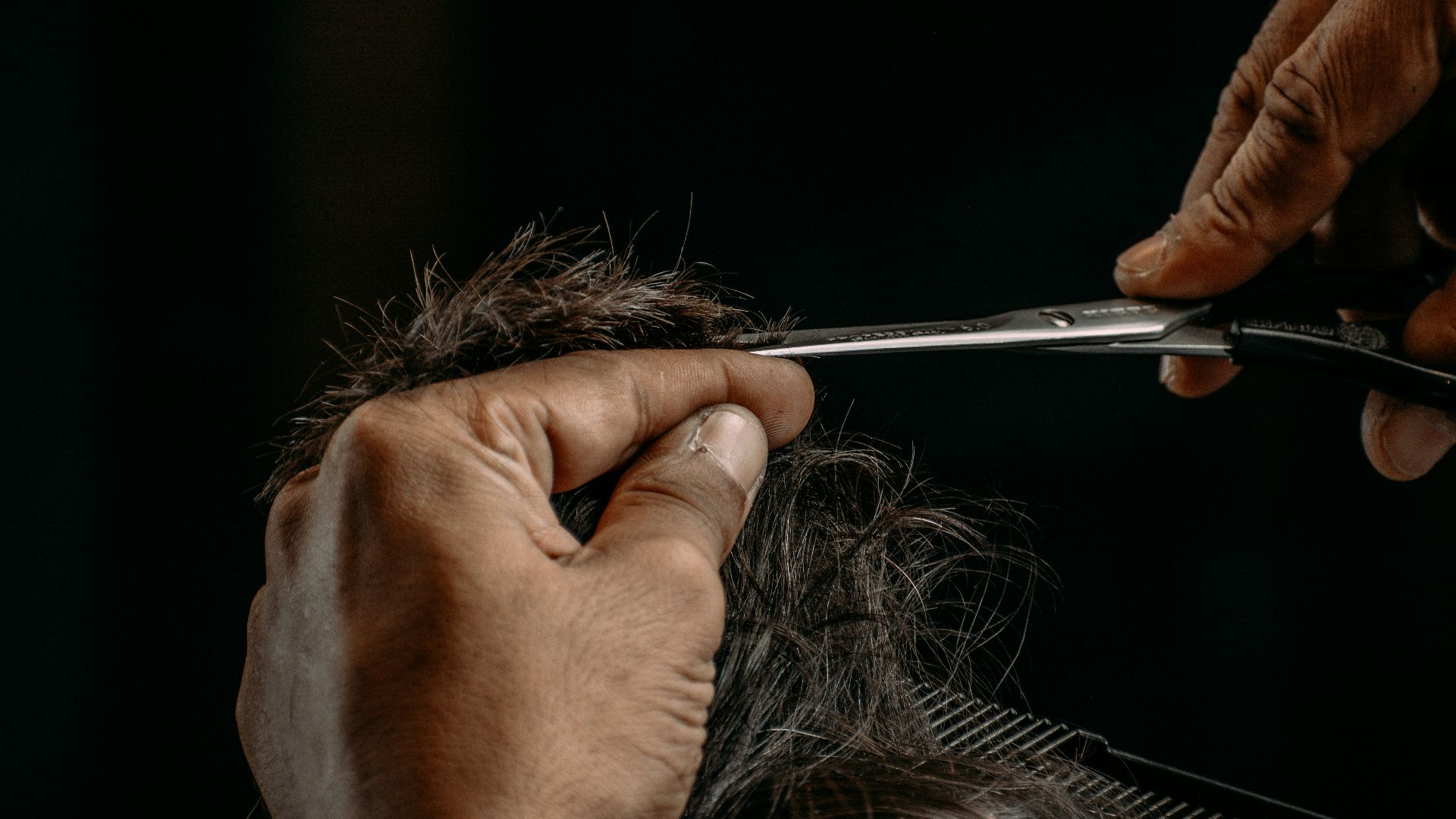 a person cutting a woman's hair with scissors