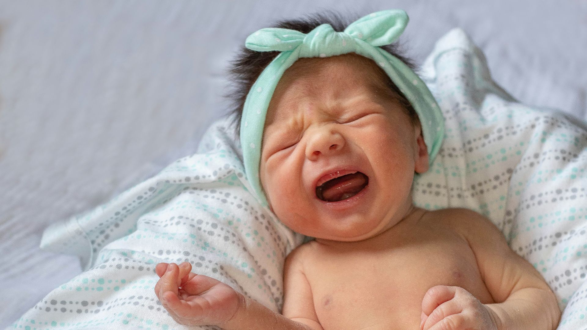 a baby crying while laying on a bed