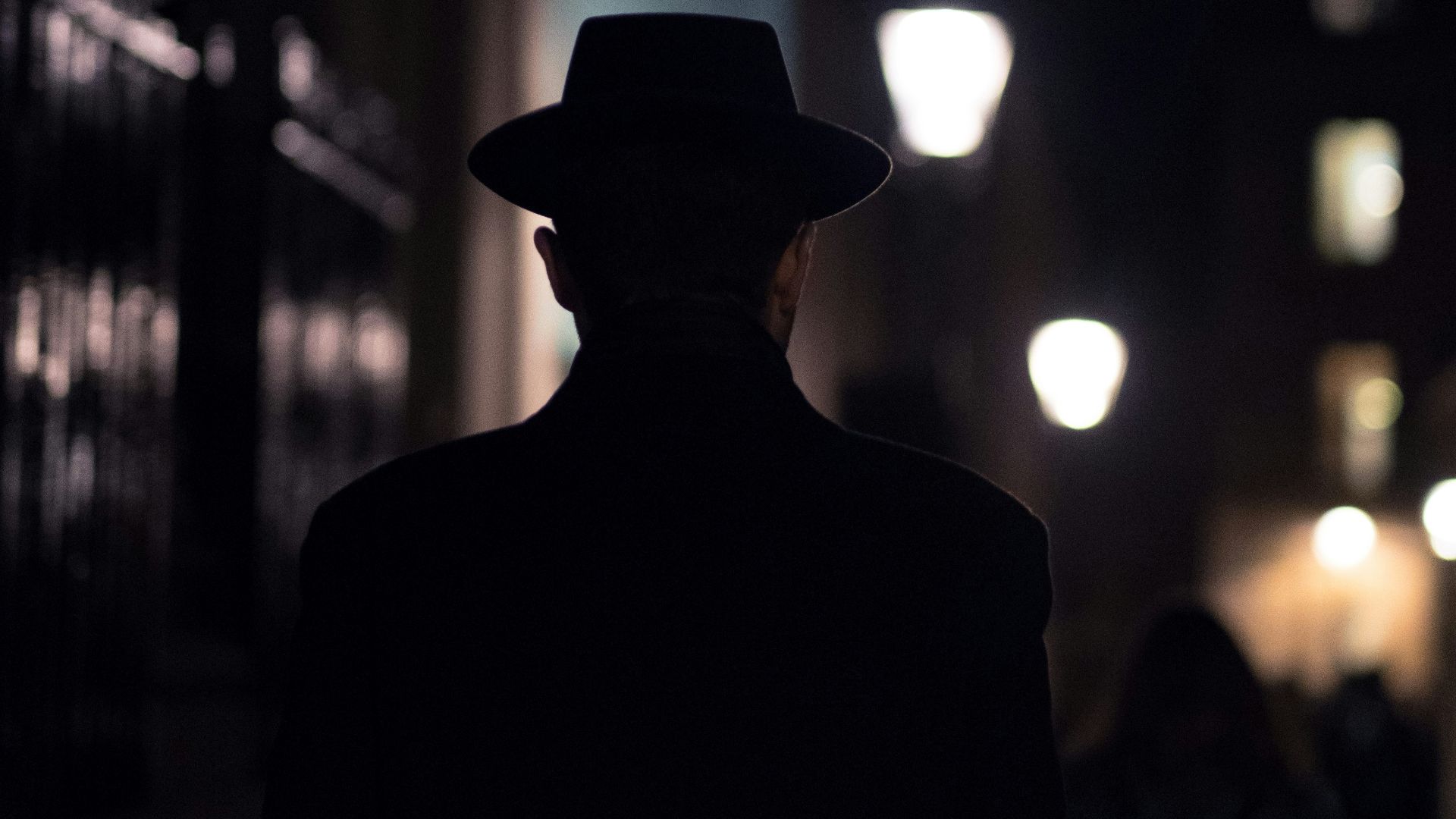man in black hat walking on sidewalk during night time