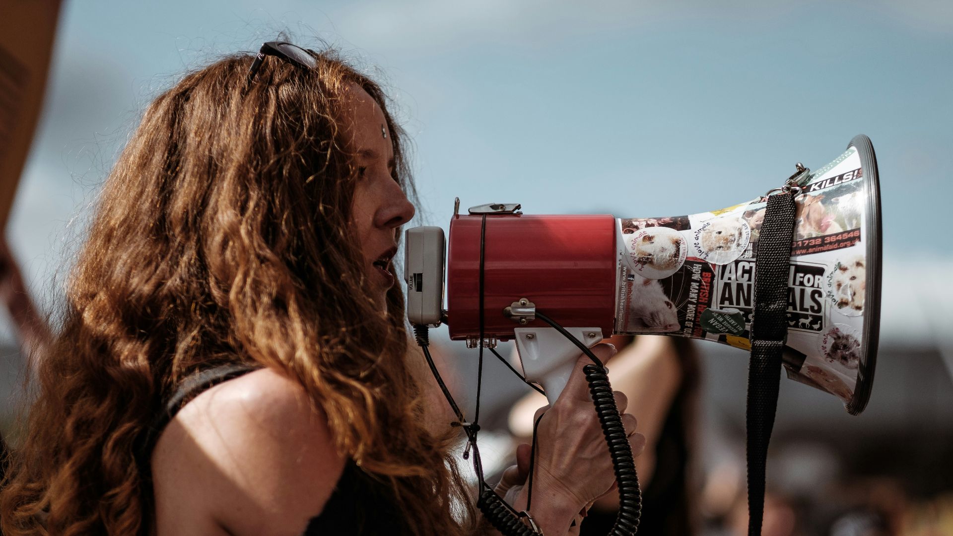 selective focus photography of woman wearing black cold-shoulder shirt using megaphone during daytime