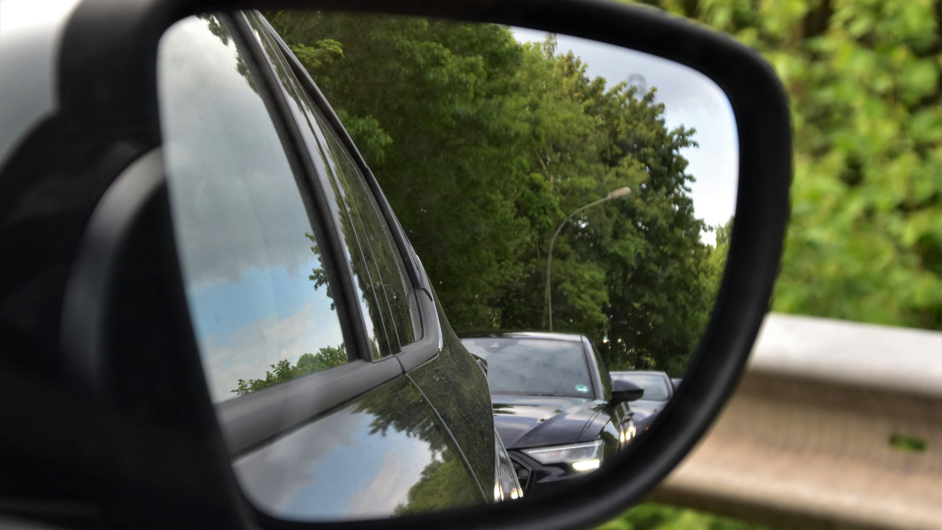 black car side mirror reflecting green trees during daytime