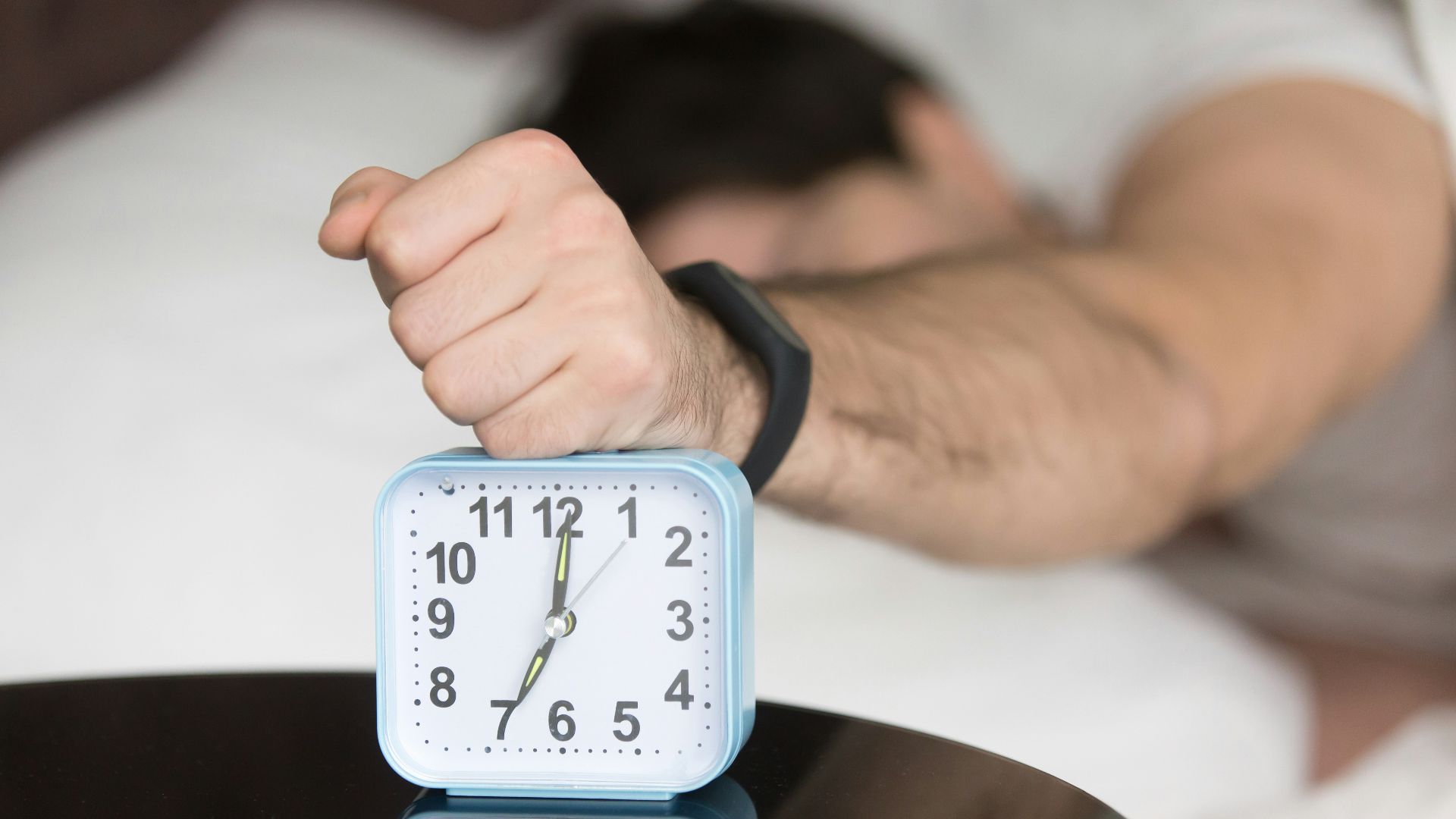 A man laying in bed with a clock on top of him