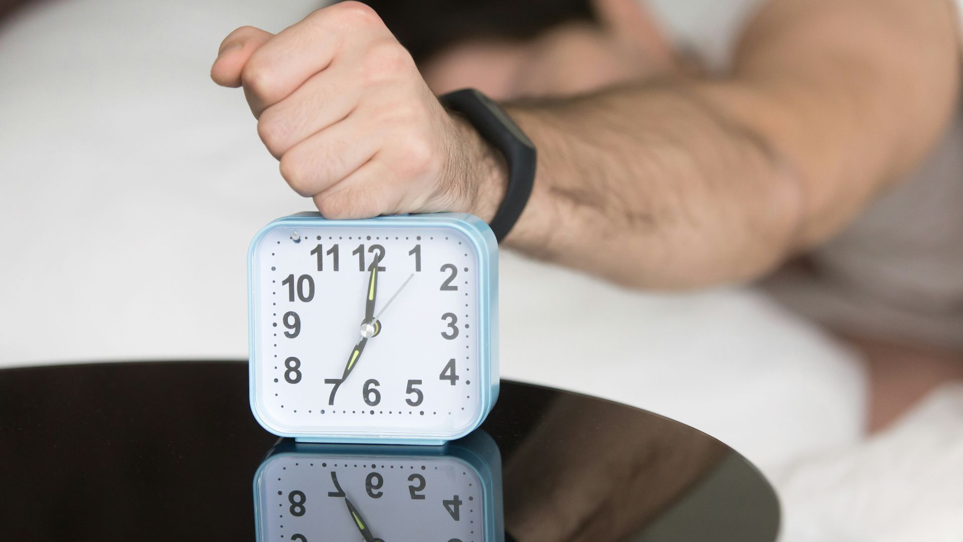 A man laying in bed with a clock on top of him