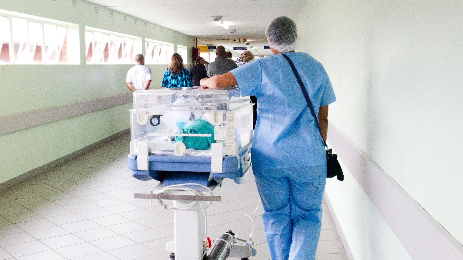 person walking on hallway in blue scrub suit near incubator