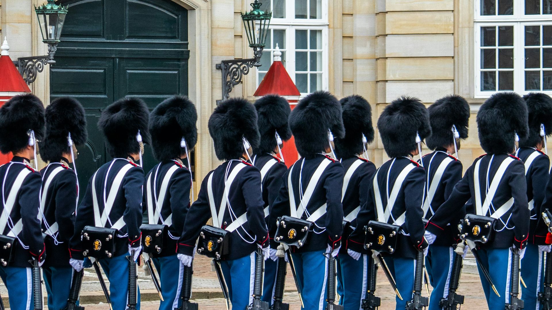 Soldiers in uniform stand in front of a building.