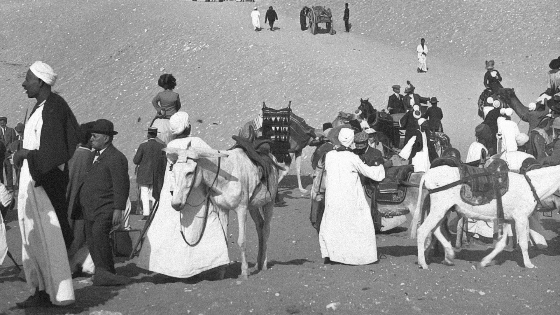 People and camels near a pyramid in the desert