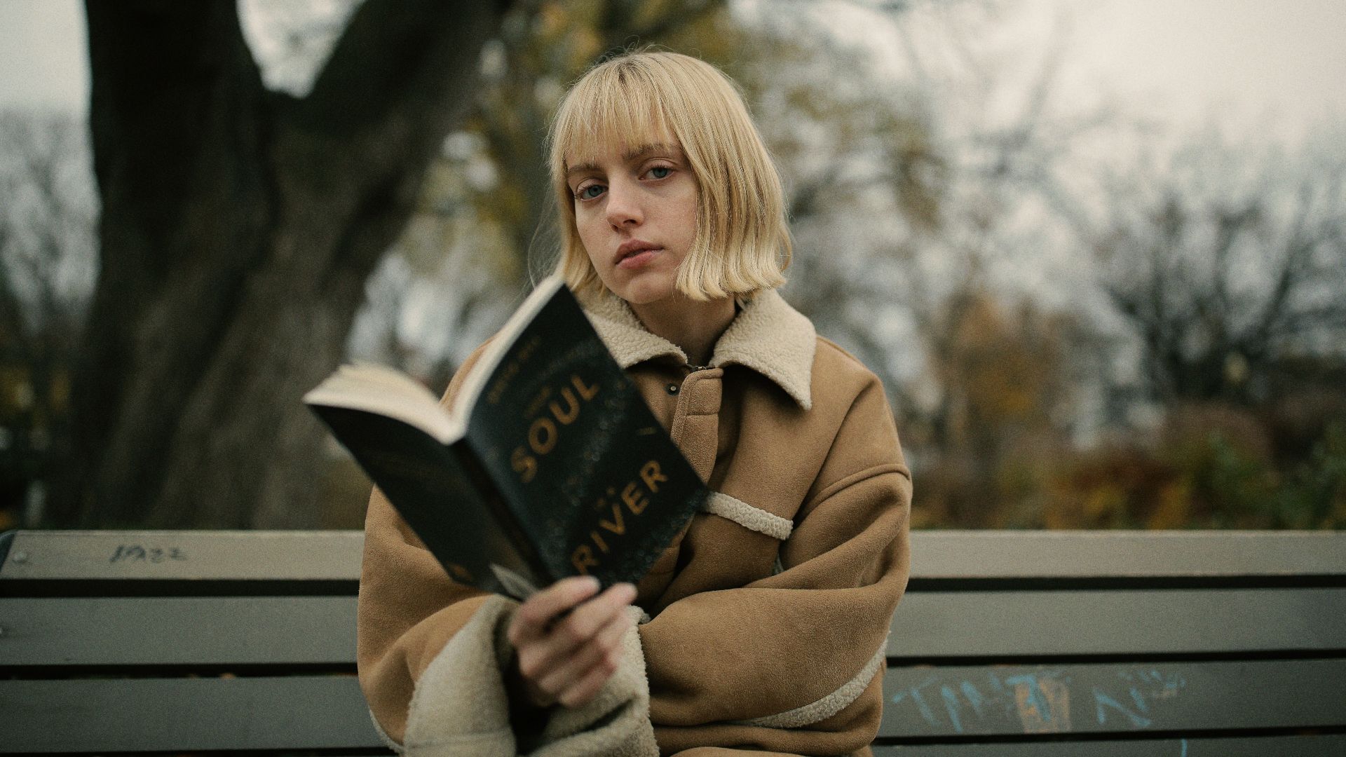 woman holding book while sitting on gray bench
