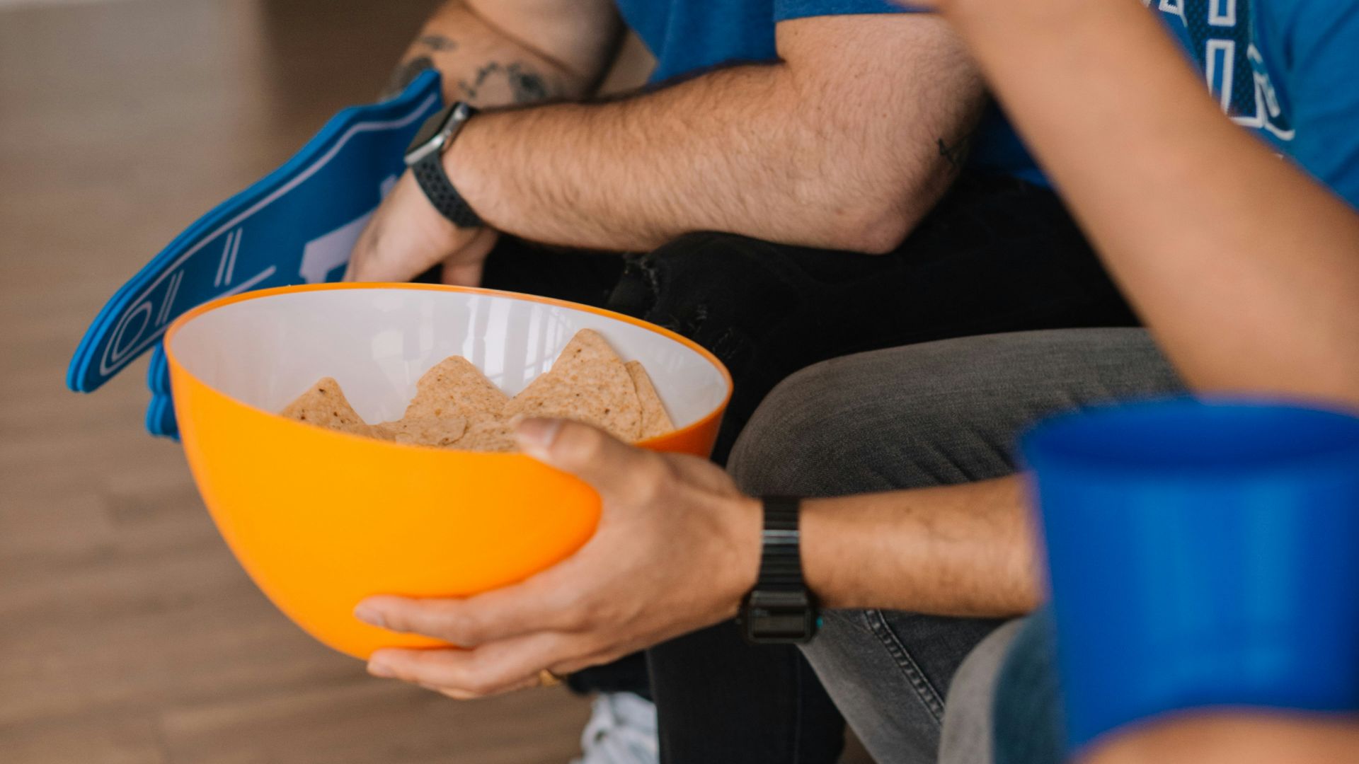 person in blue NBA Dallas Mavericks crew neck shirt sitting while holding bowl with potato chips