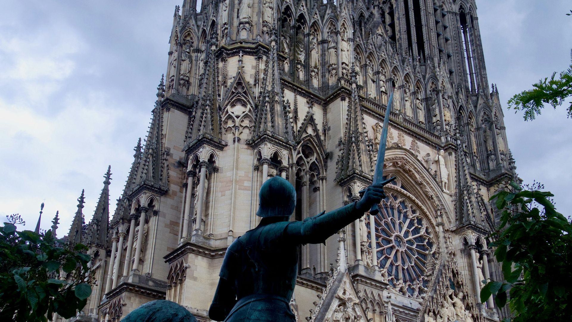 Statue in front of a gothic cathedral under cloudy sky