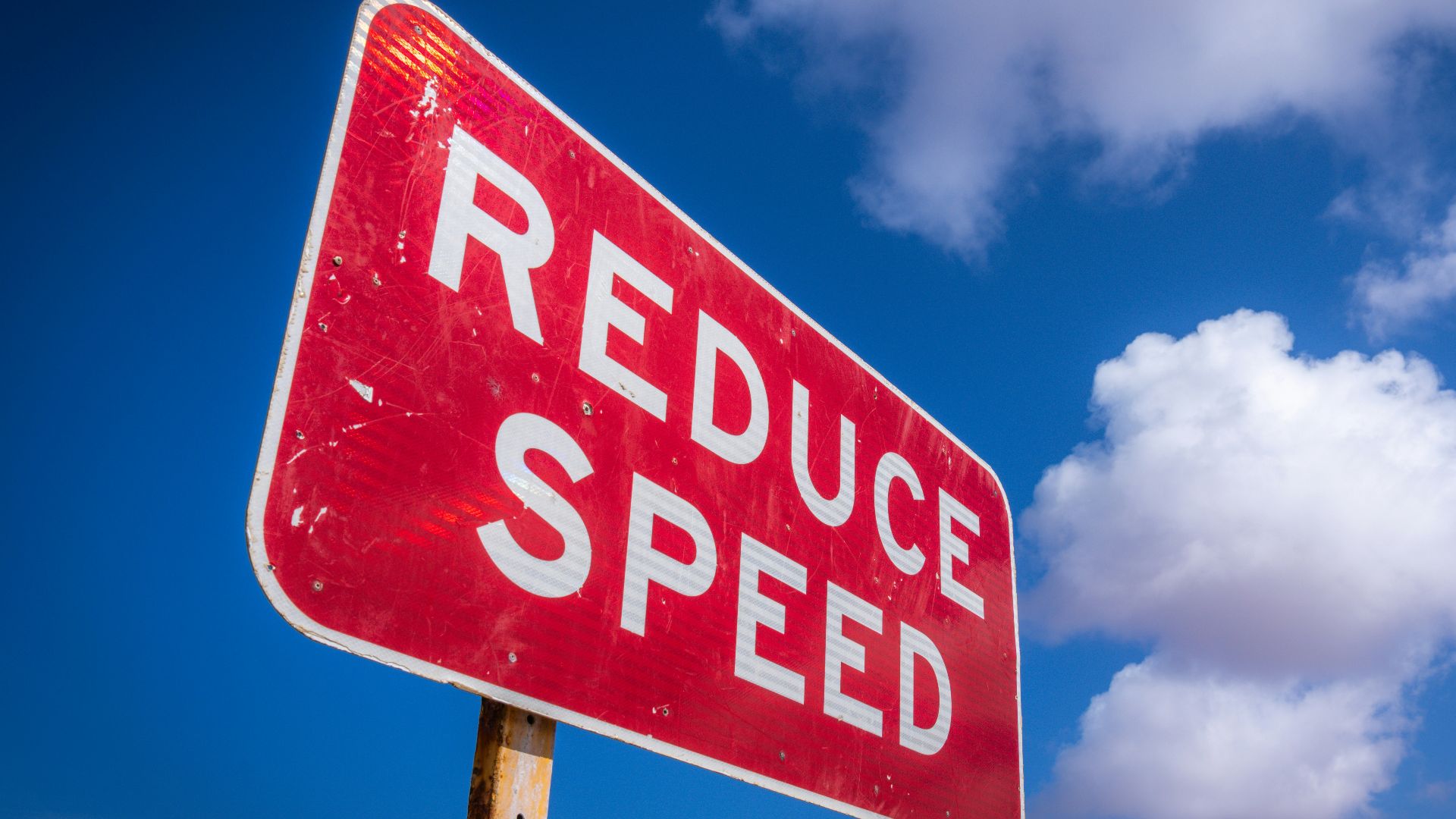 Red reduce speed sign against blue sky
