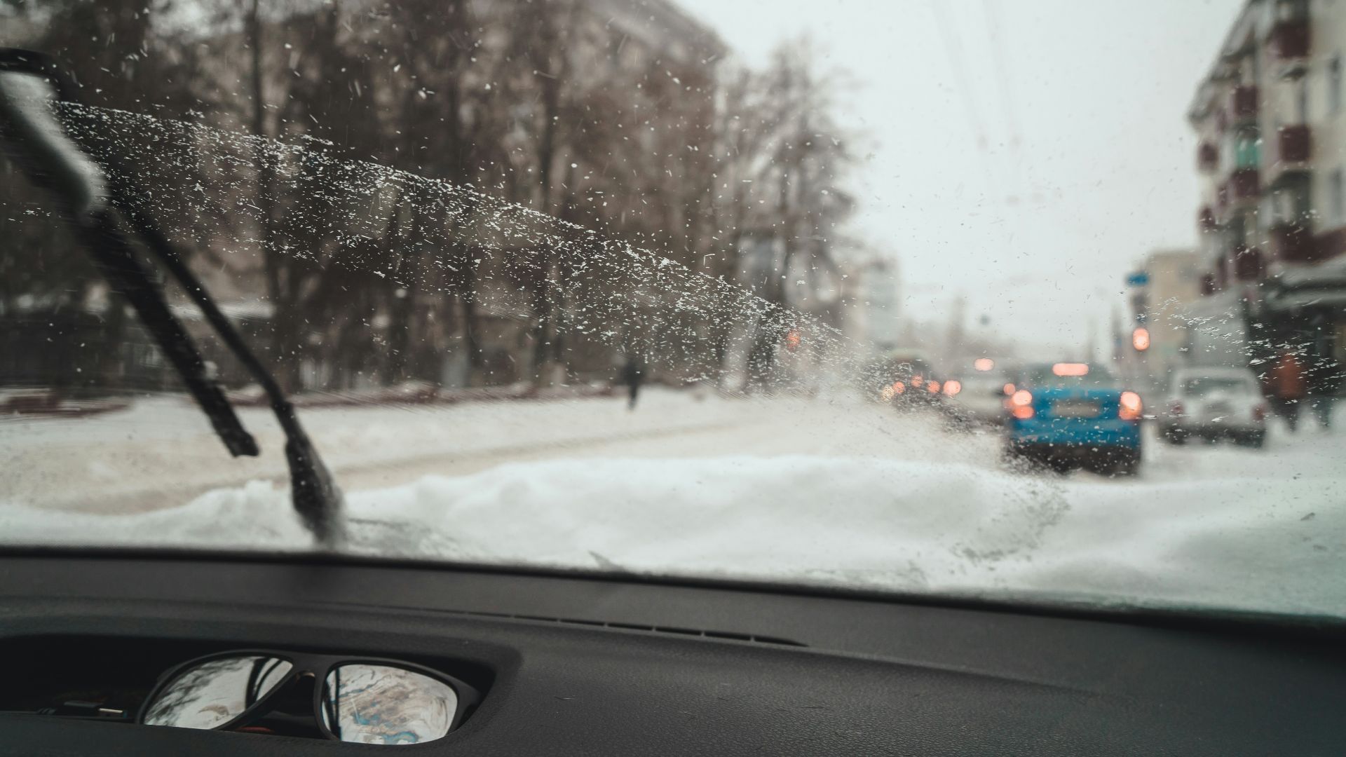 a view of a snowy street from inside a car
