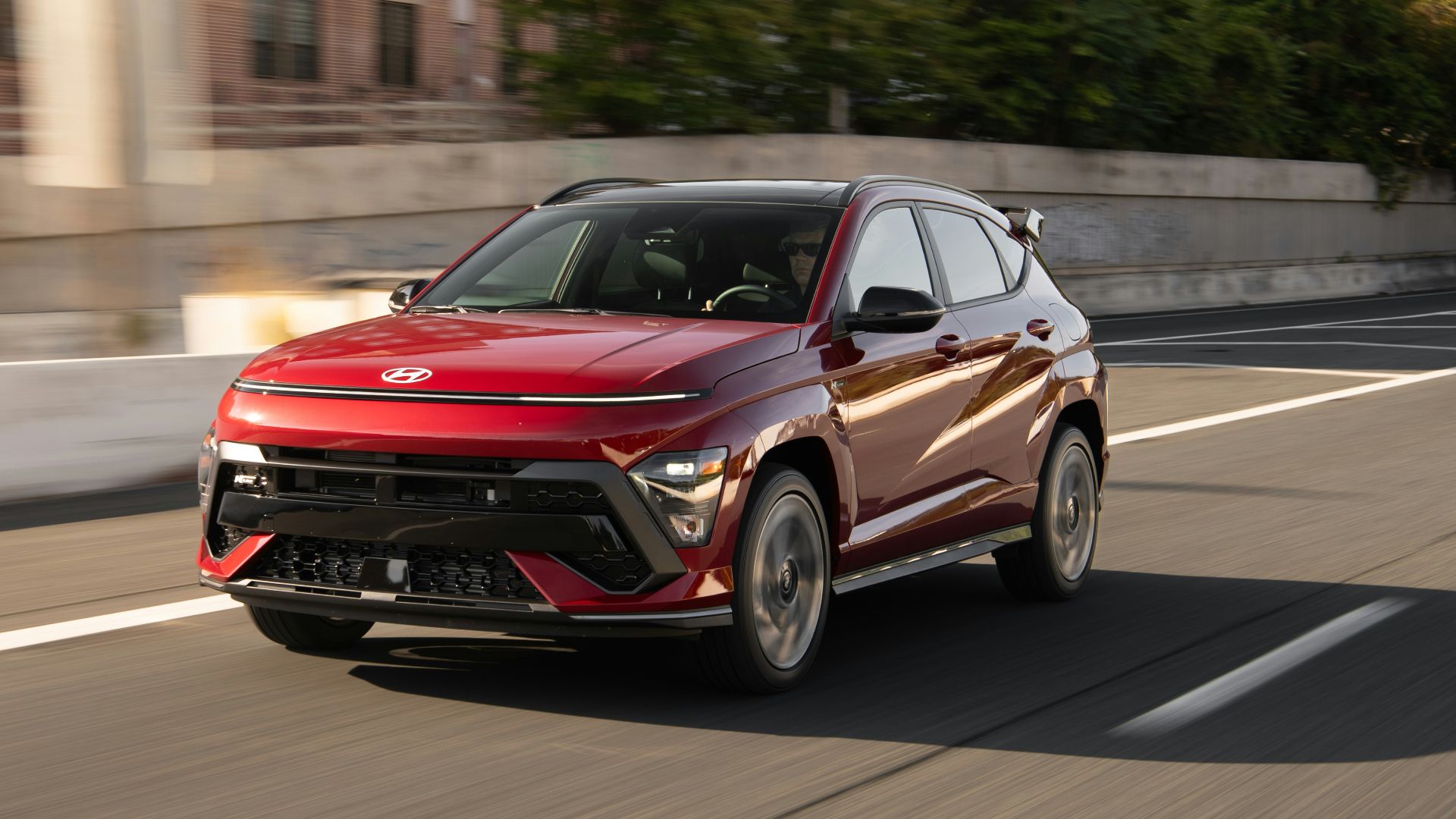 A red car driving down a street next to a building