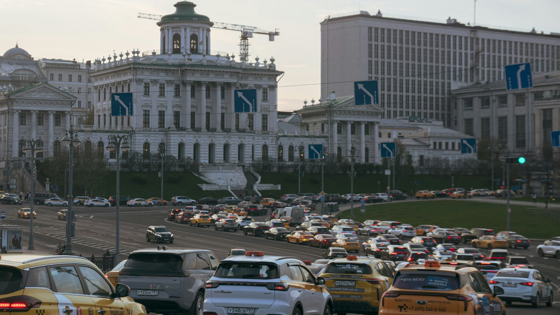 Cars driving past a large classical building.