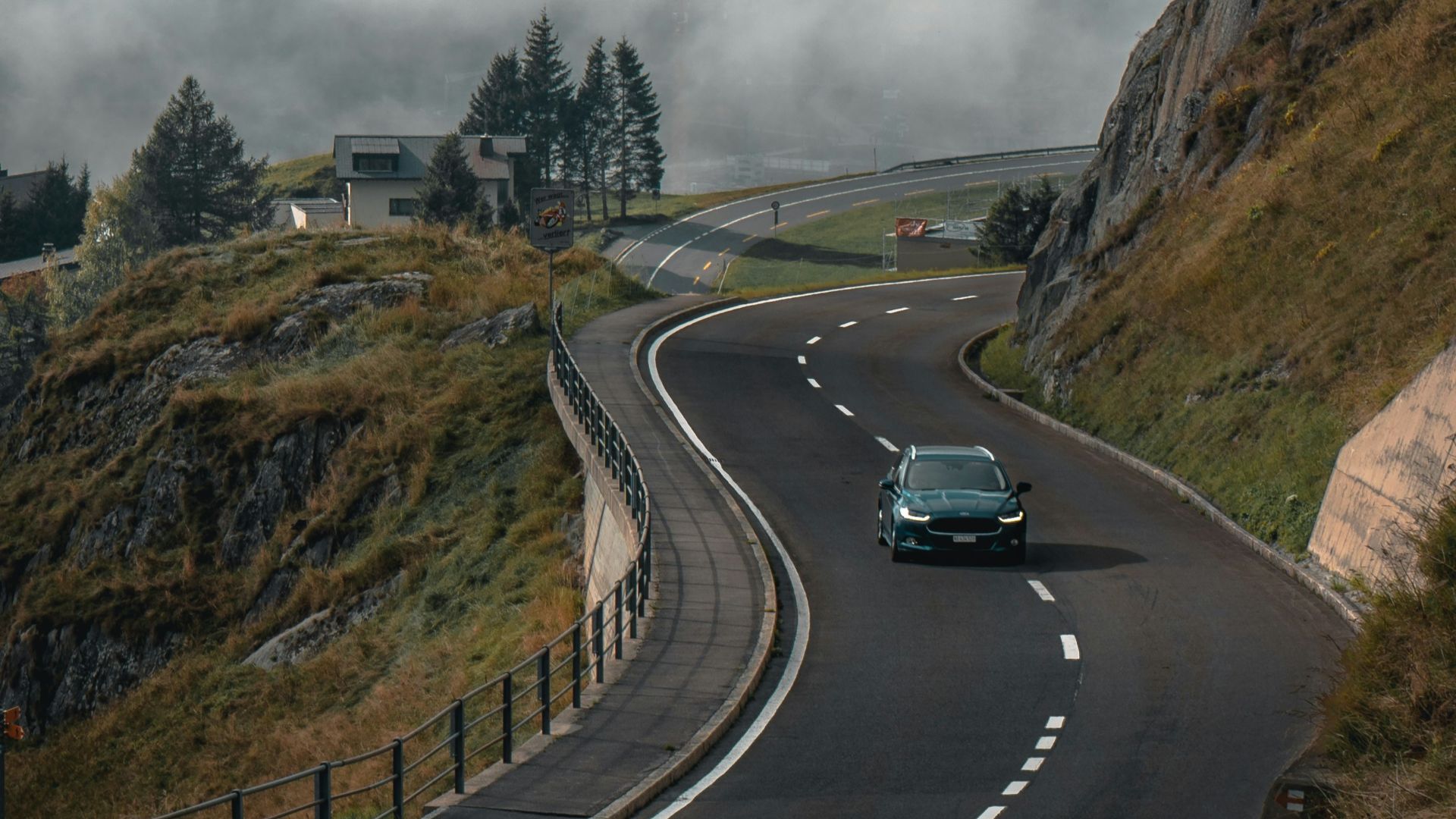 a car driving down a winding road under a cloudy sky