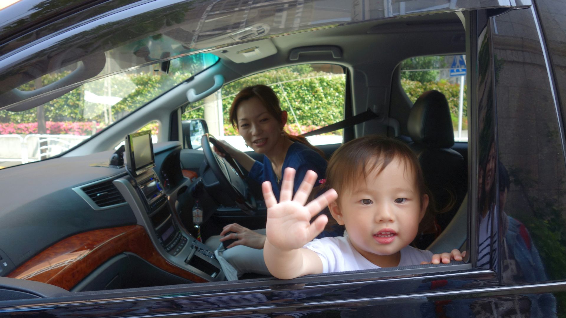 Child waves from car window with mother driving