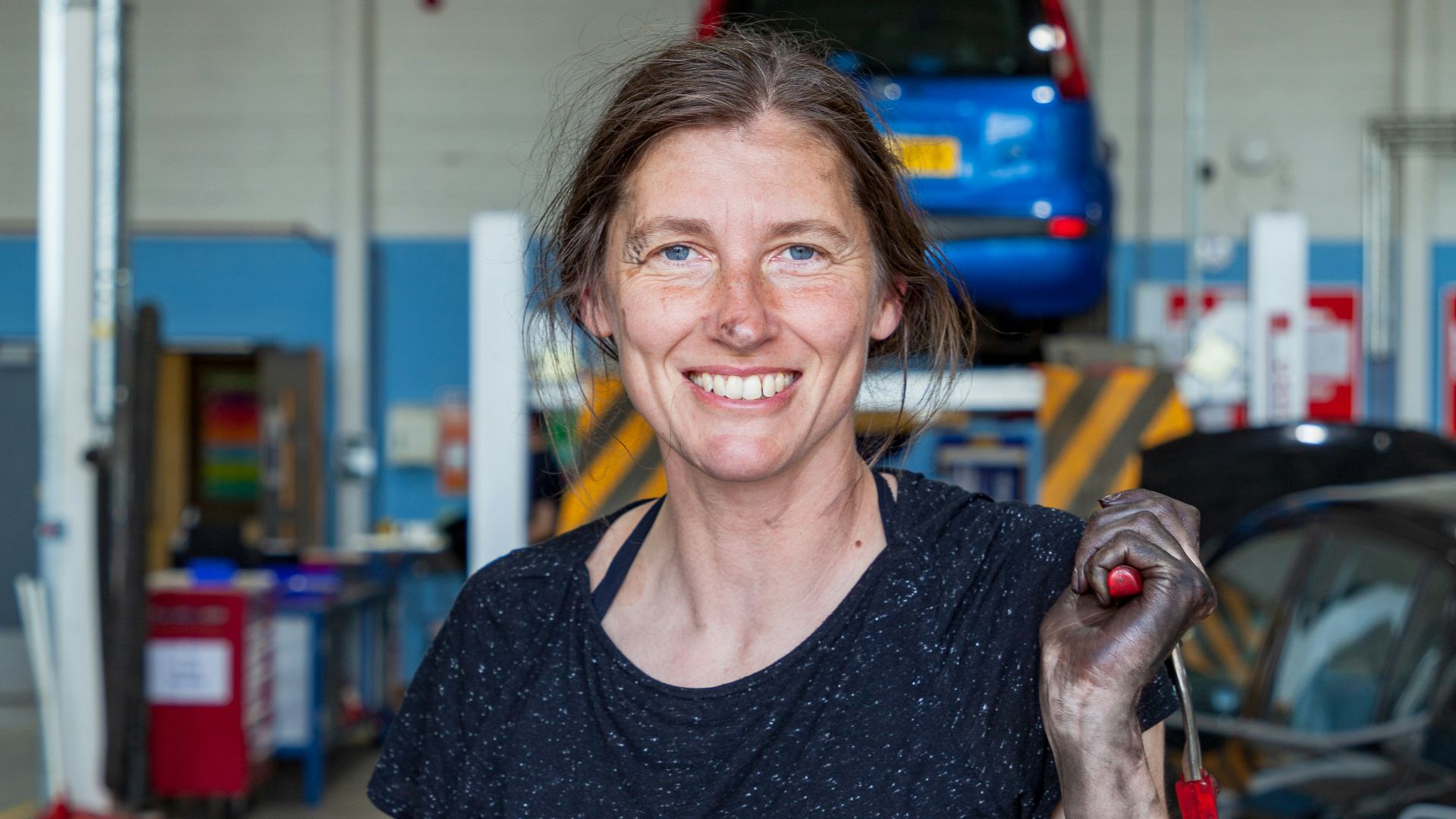a woman holding a wrench in a garage