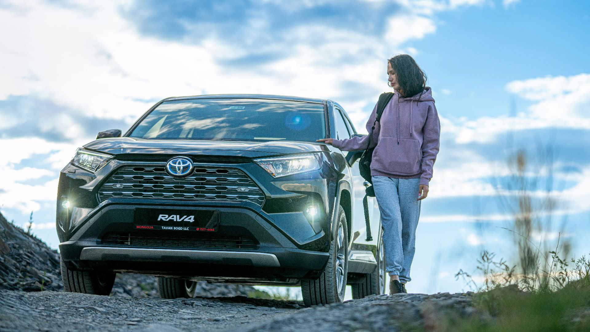 A woman standing next to a car on a dirt road