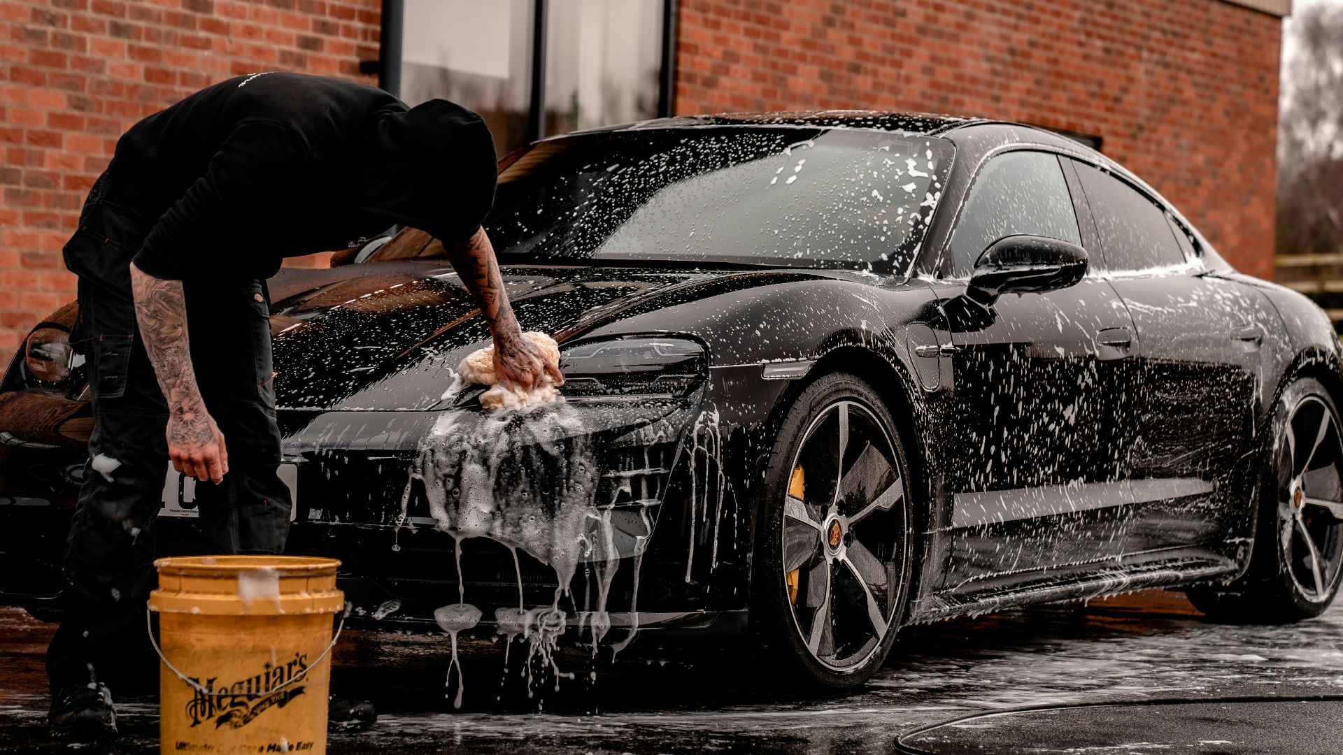 man in black t-shirt and black pants doing water splash on black coupe during daytime