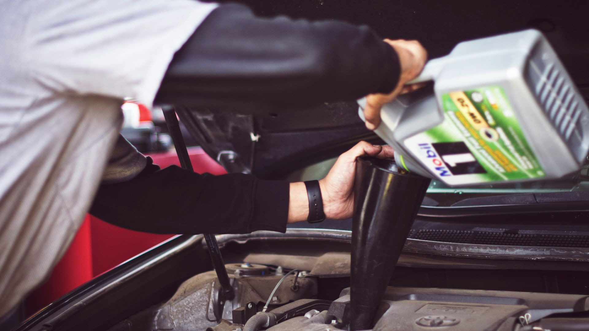 man refilling motor oil on car engine bay