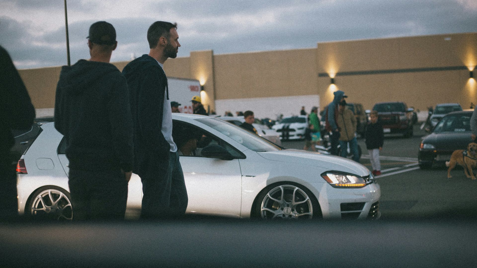 man in black suit standing beside white sedan