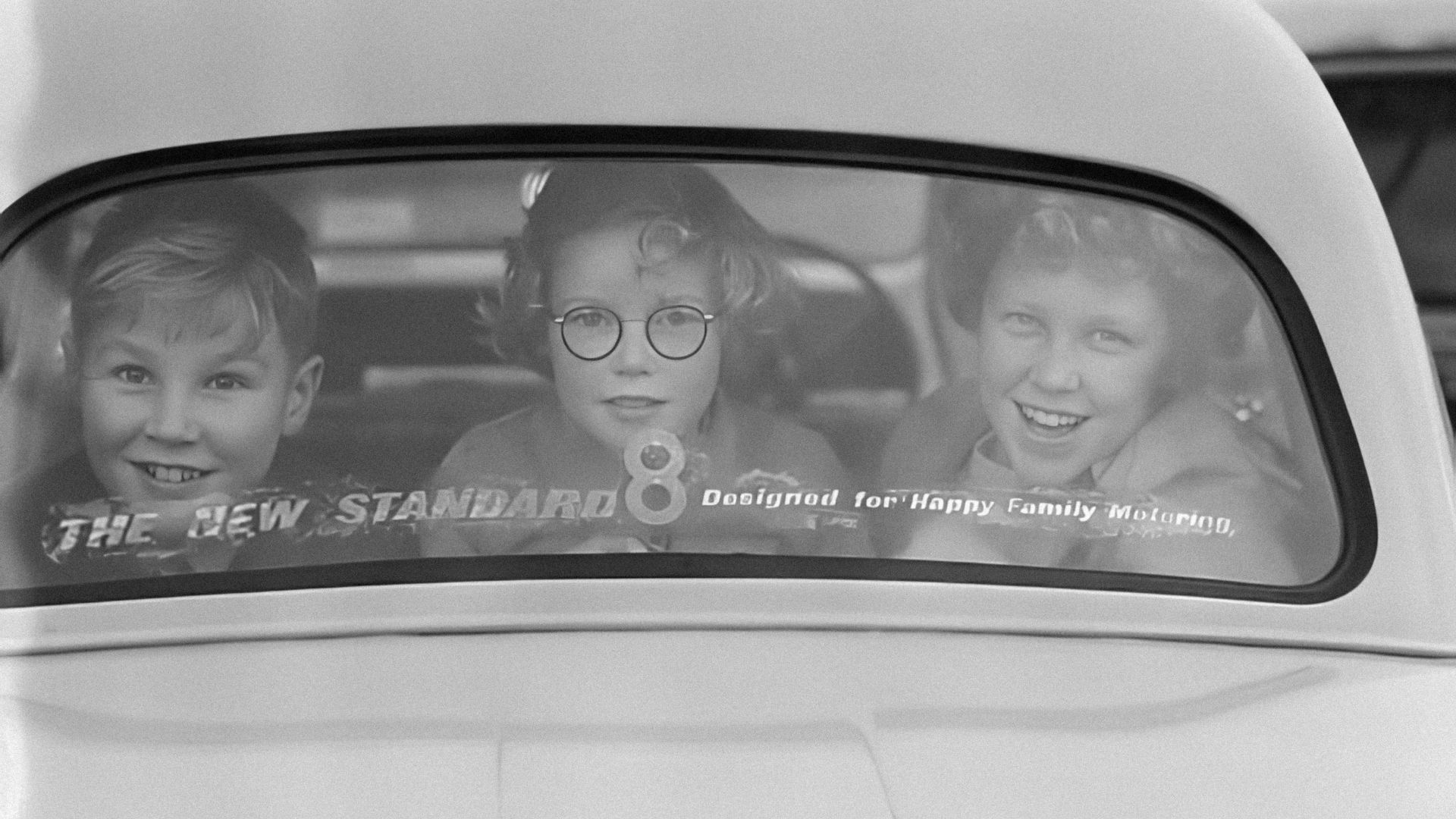a black and white photo of three children in a car