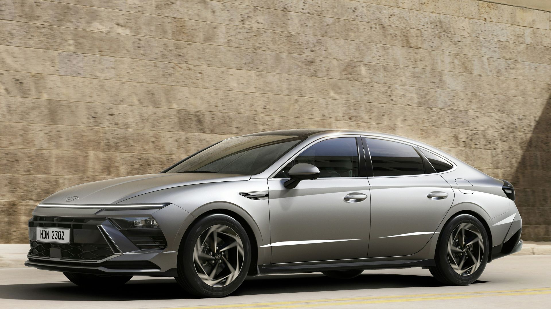 A silver car driving down a street next to a building