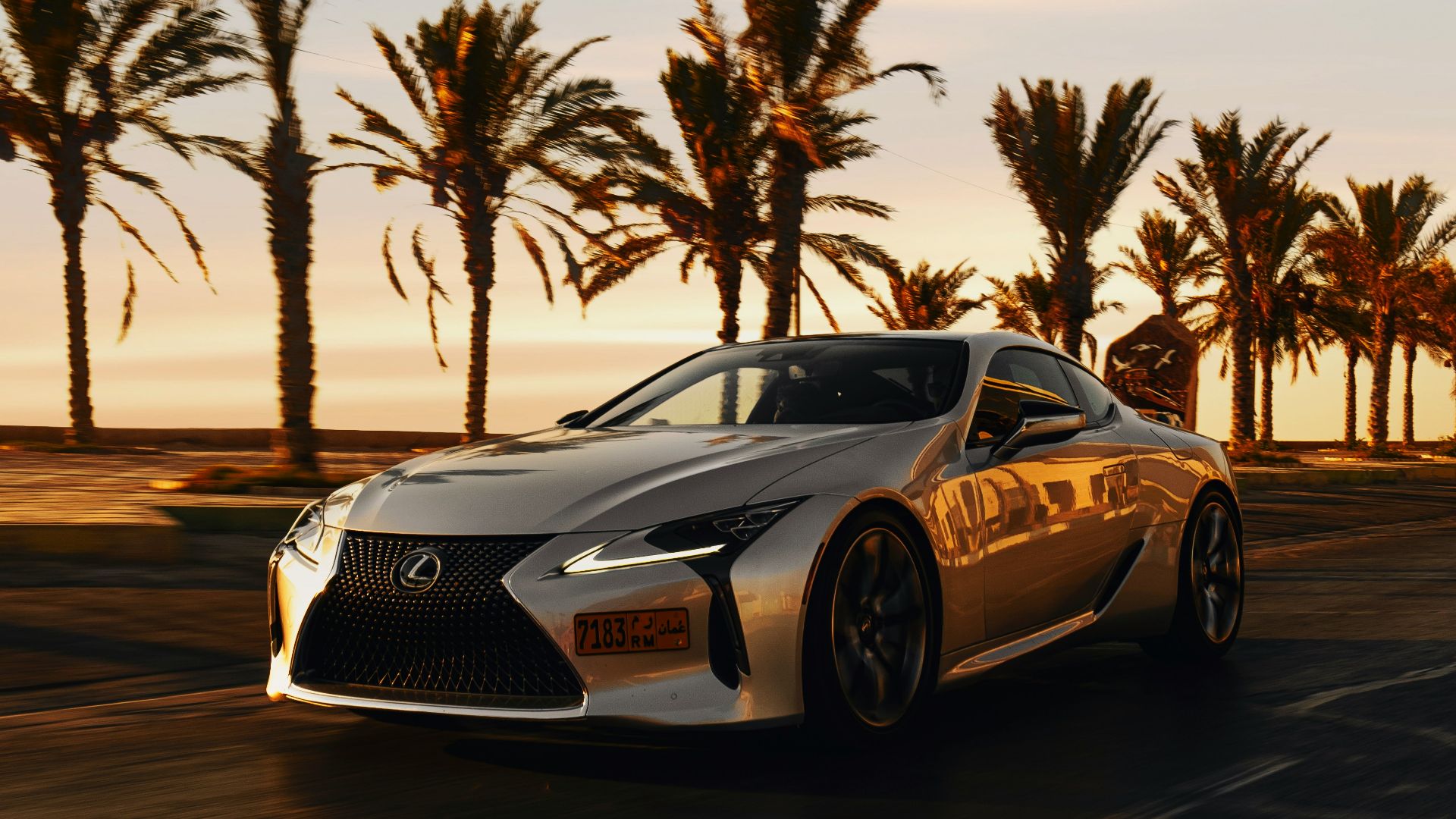 a silver sports car driving down a street next to palm trees