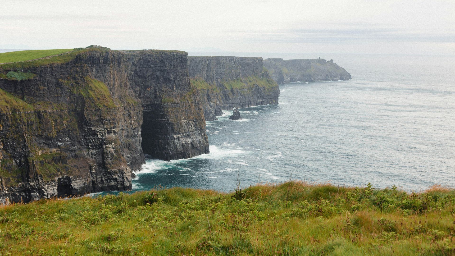 a grassy field next to a cliff with a body of water