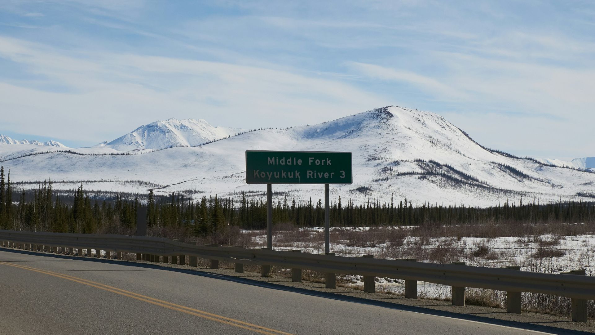 A road sign sits against snowy mountains.