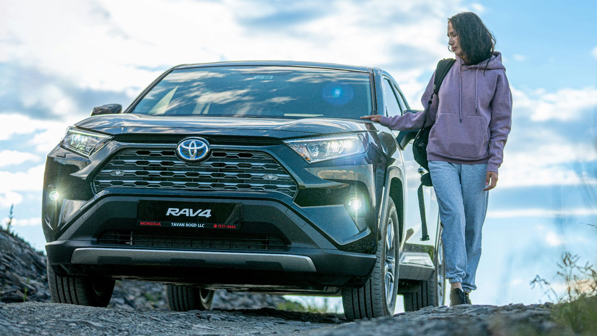 A woman standing next to a car on a dirt road